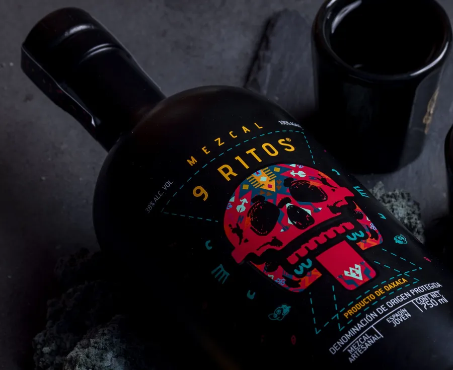 A bottle of Mezcal 9 Ritos on volcanic stone with two black clay cups